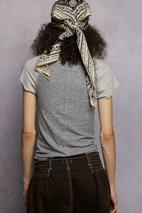 Person wearing a gray t-shirt and dark pants with a patterned headscarf on a plain background