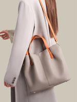 Person holding a gray handbag with orange handles against a neutral background
