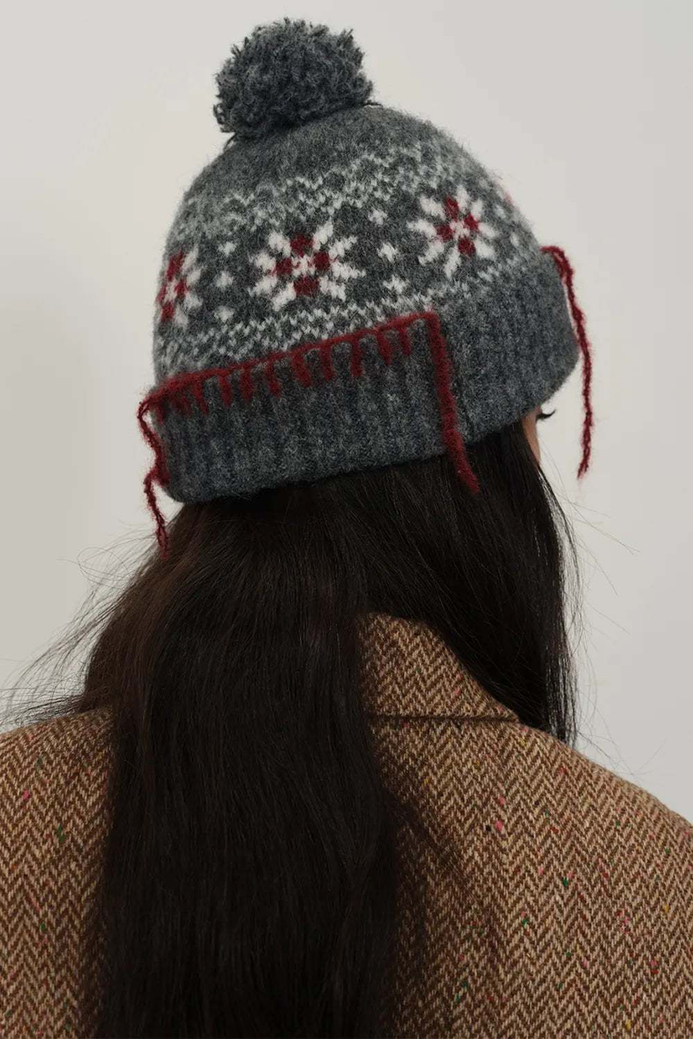 Person wearing a gray knitted hat with a pom-pom and red accents, against a plain background.