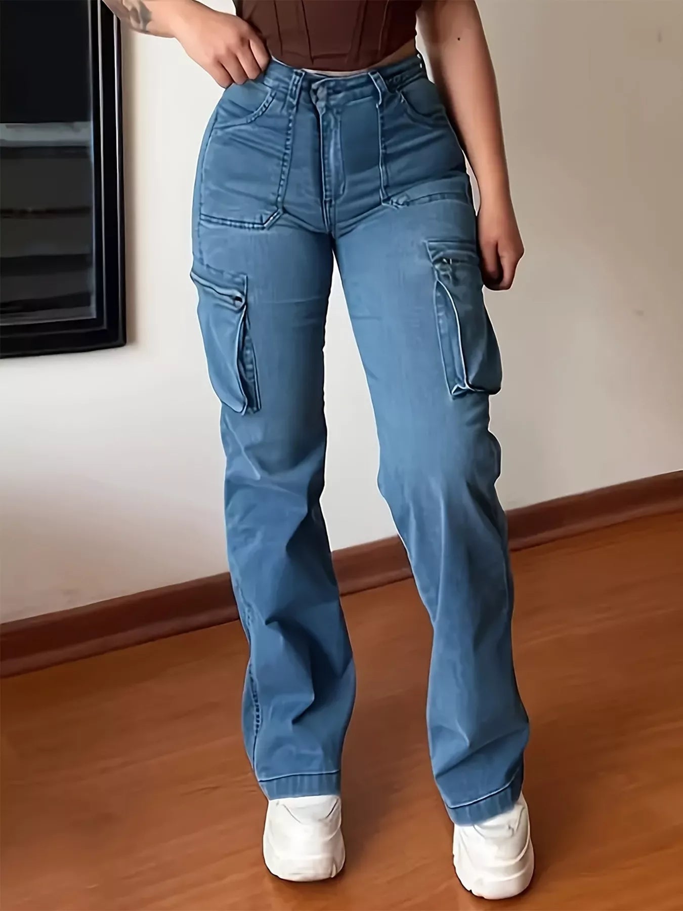 Person wearing blue cargo pants and white sneakers in a room with wooden floor and white wall.