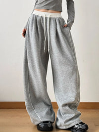 Person wearing gray sweatpants with white drawstring and trim on a plain background