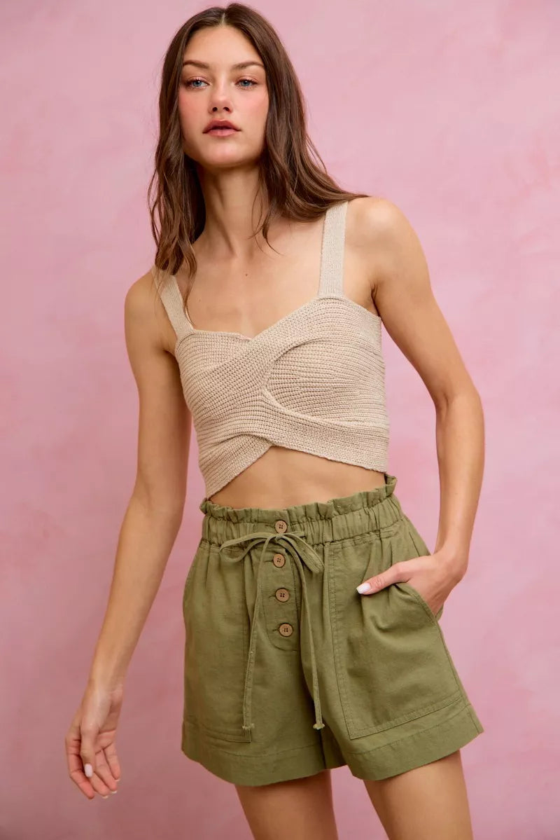Woman wearing a beige top and green shorts against a pink background