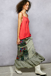 Woman wearing a red top and long, patterned skirt with white boots against a gray background