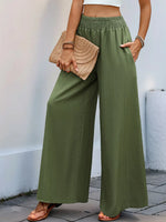 Person wearing green wide-leg pants holding a beige clutch against a light background