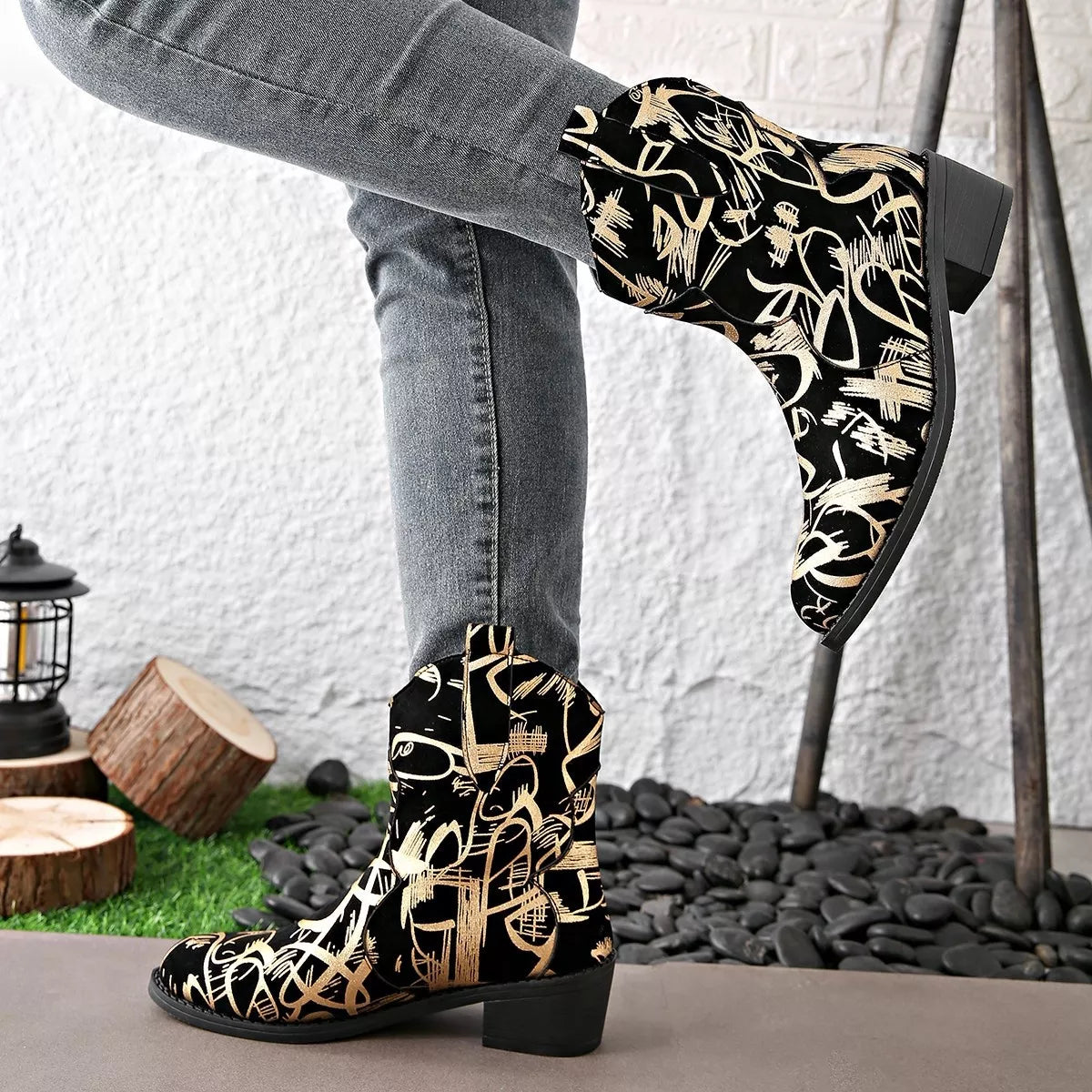 Black and gold patterned boots worn with gray jeans against a white wall.
