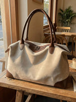 Beige handbag with brown accents on a wooden surface in a cozy indoor setting.