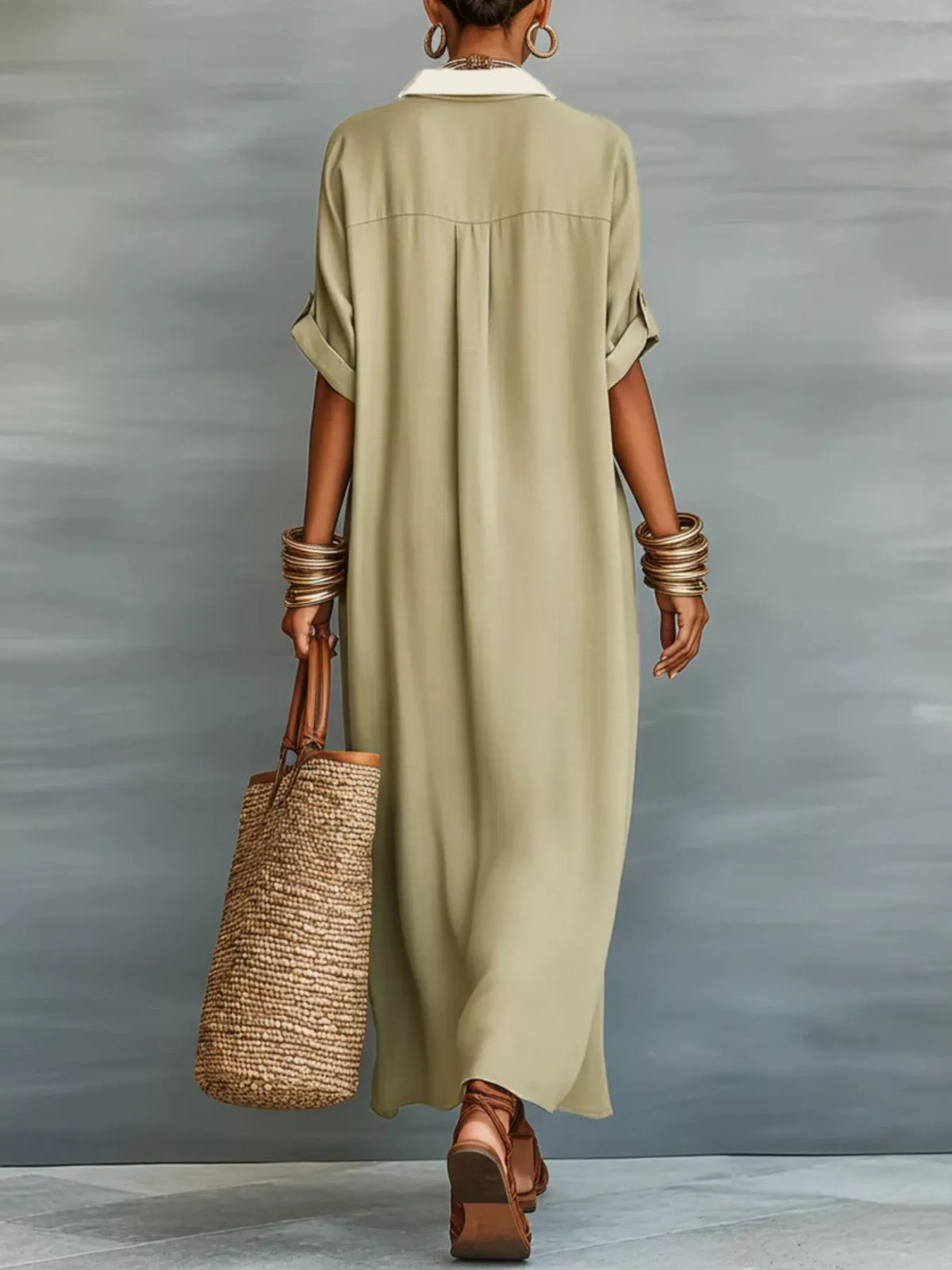 A woman shown from behind wearing a loose, knee-length olive green shirt dress with rolled sleeves and a white collar. She is holding a woven straw tote bag and wearing stacked gold bracelets and brown sandals, set against a textured gray studio background.