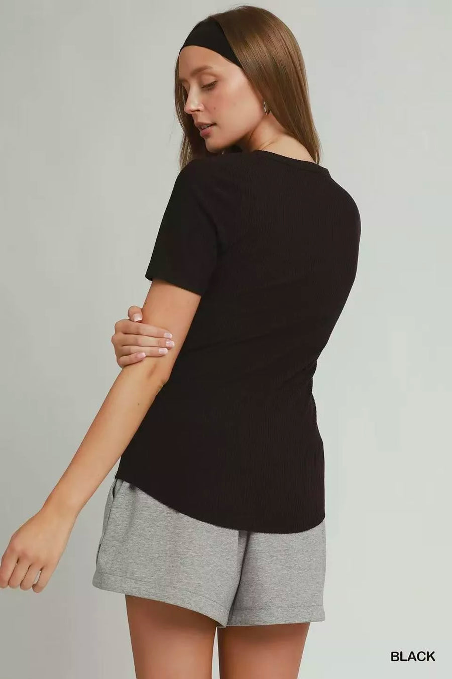 Woman wearing a black t-shirt and gray shorts on a plain background