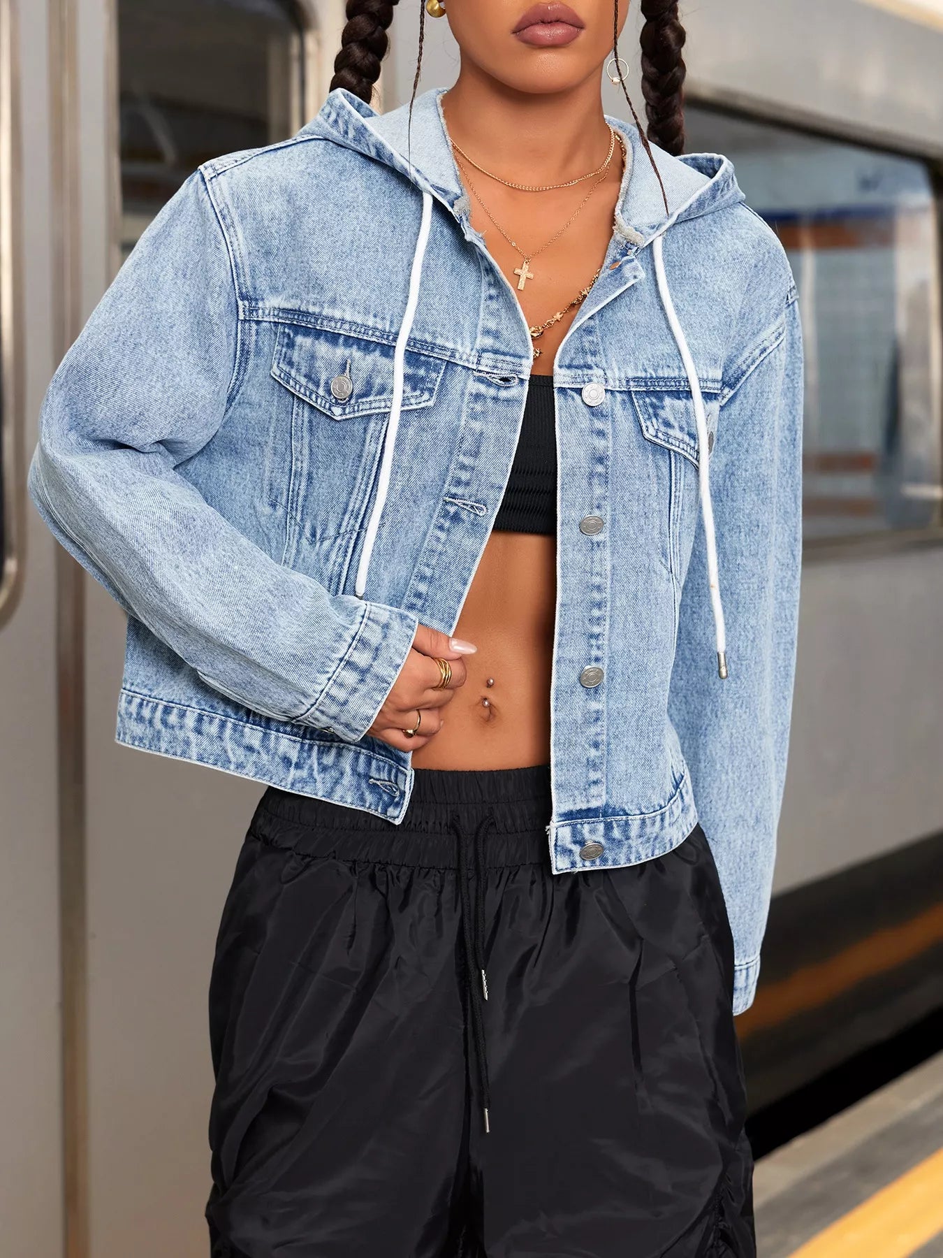 Person wearing a light blue denim jacket over a black top and pants on a train platform.