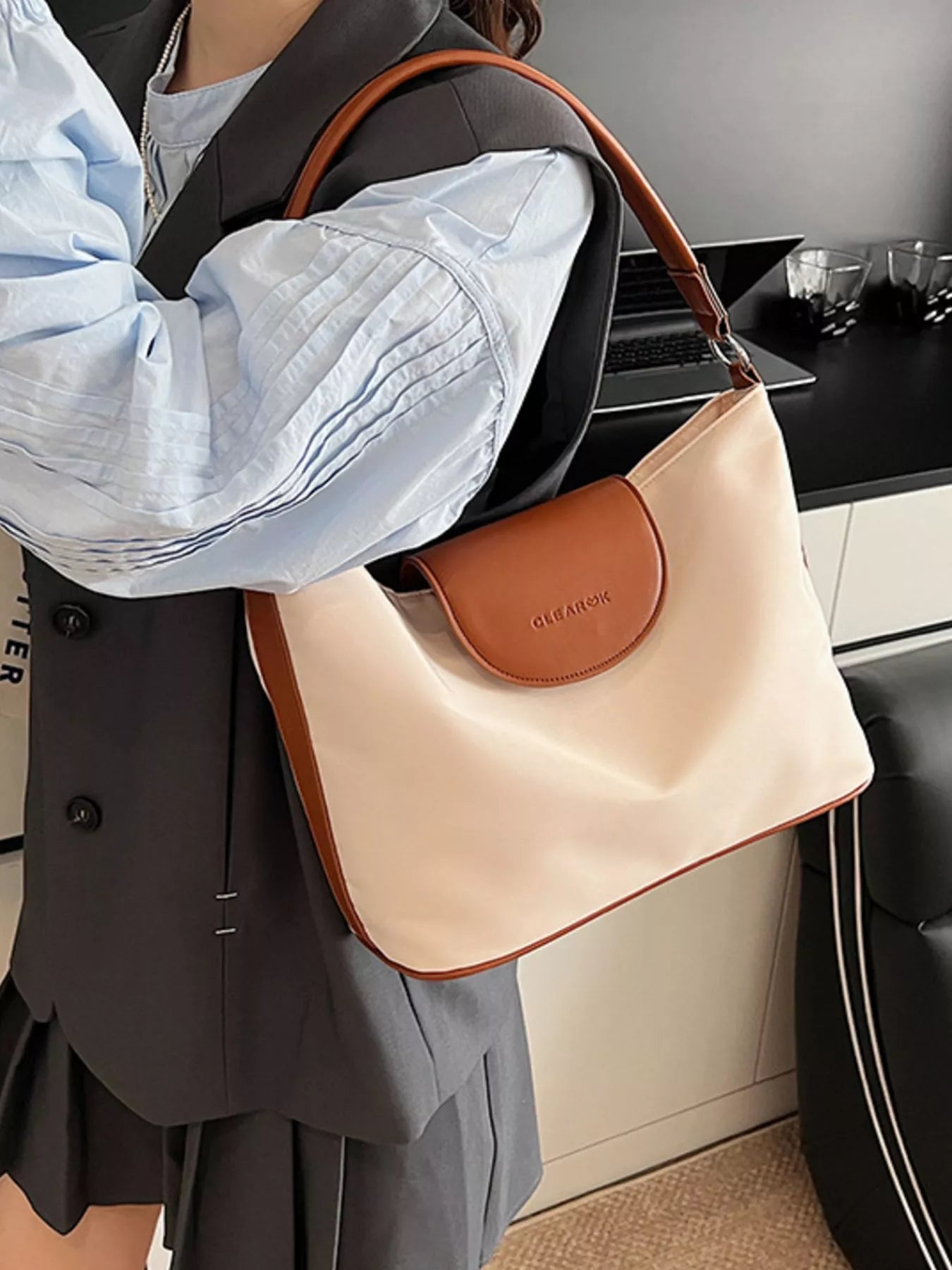 Person holding a beige handbag with brown accents indoors.