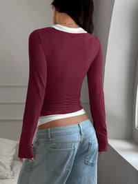 Person wearing a burgundy long-sleeve top and blue jeans in a neutral setting