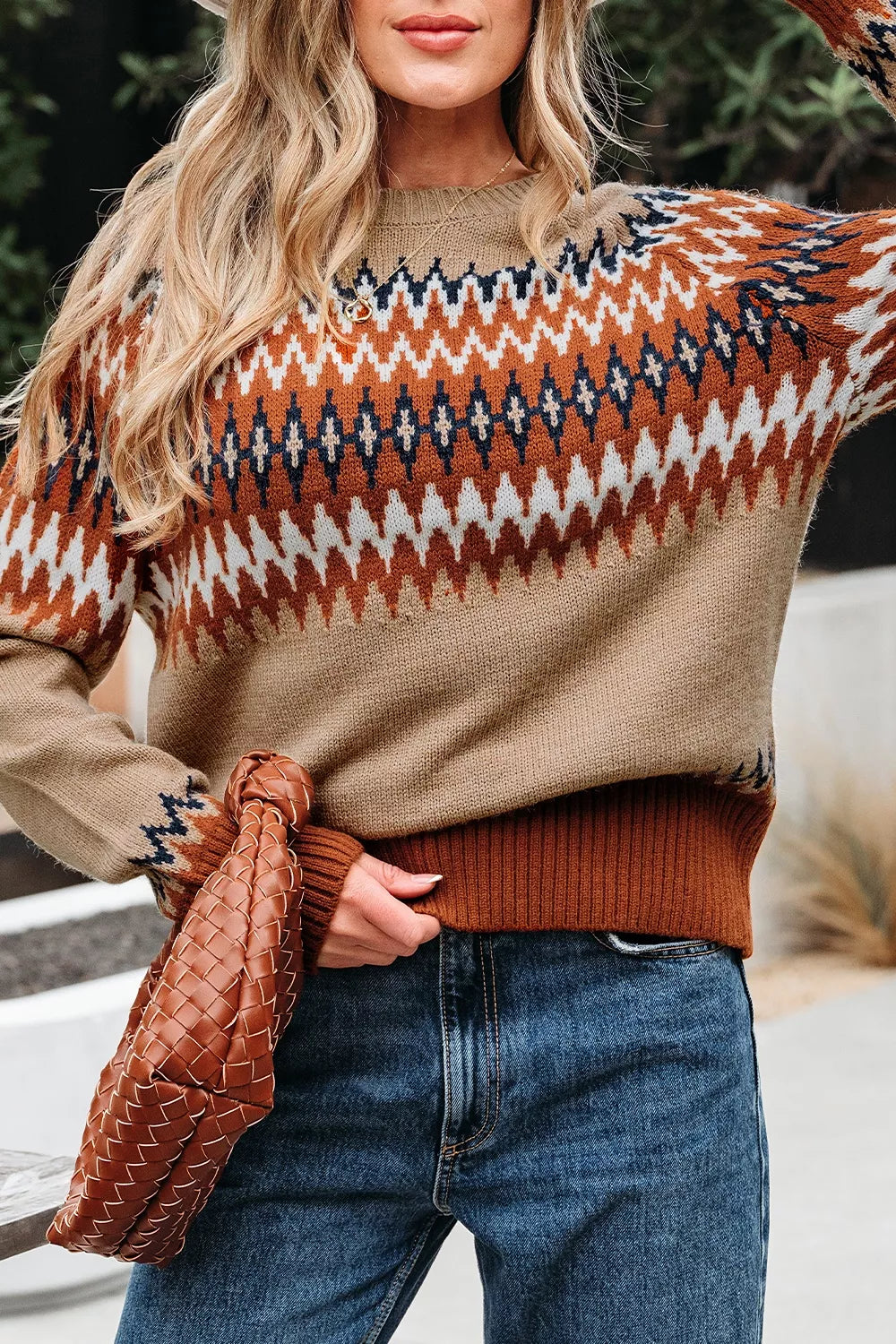 Person wearing a patterned sweater with a brown leather jacket and jeans.