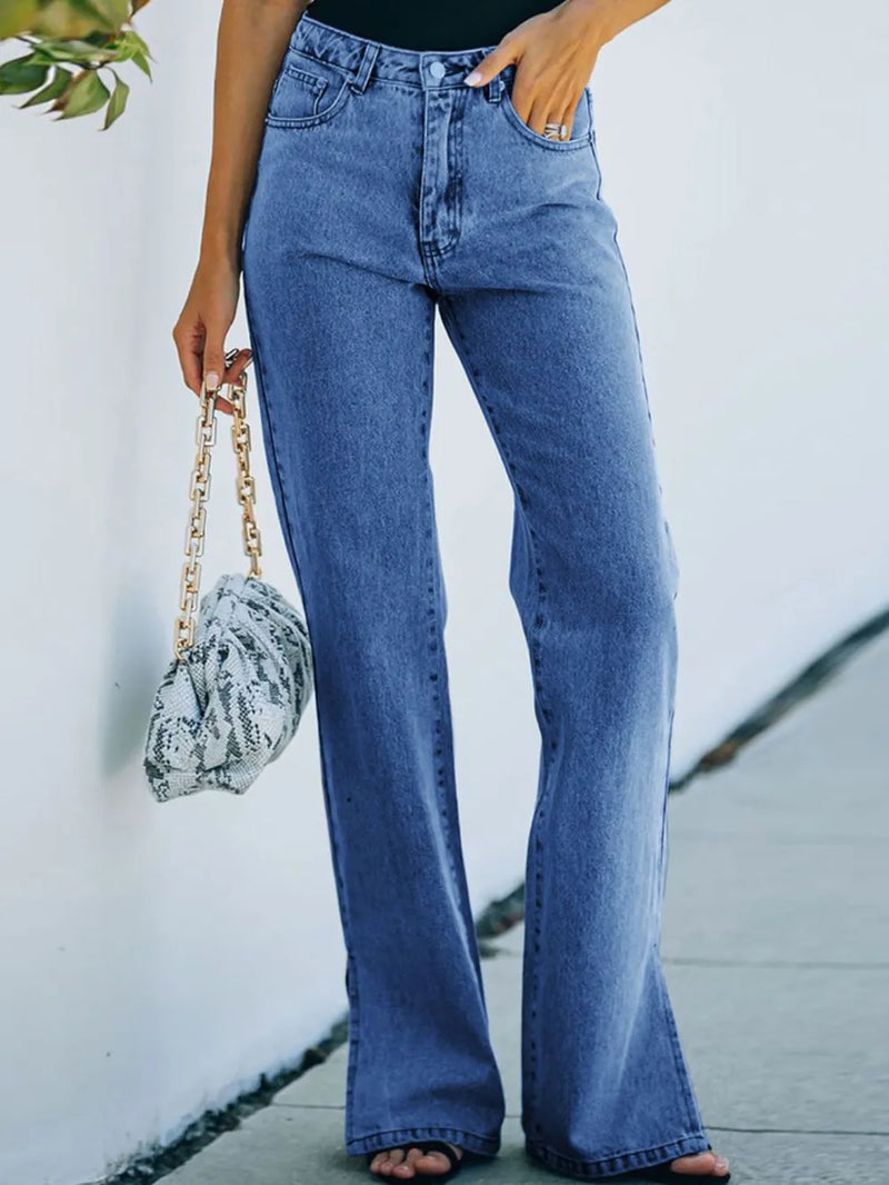 Person wearing blue jeans holding a patterned handbag against a light background