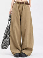 A model wearing high-waisted, wide-leg khaki pants with a brown belt, styled with black clogs and holding a black-and-white checkered tote bag against a plain white background.