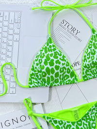 Green leopard print bikini on a white surface with a keyboard and papers.