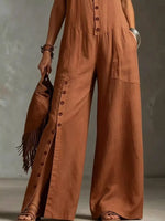 Person wearing a brown jumpsuit holding a fringed bag against a neutral background