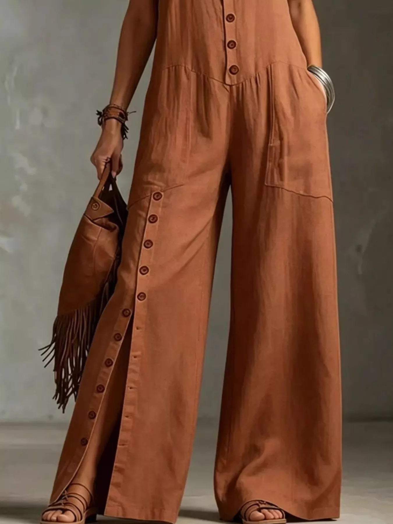 Person wearing a brown jumpsuit holding a fringed bag against a neutral background