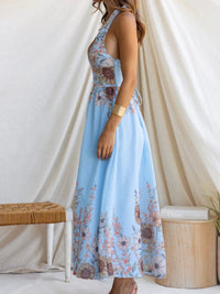 Woman wearing a blue floral dress standing against a white curtain.