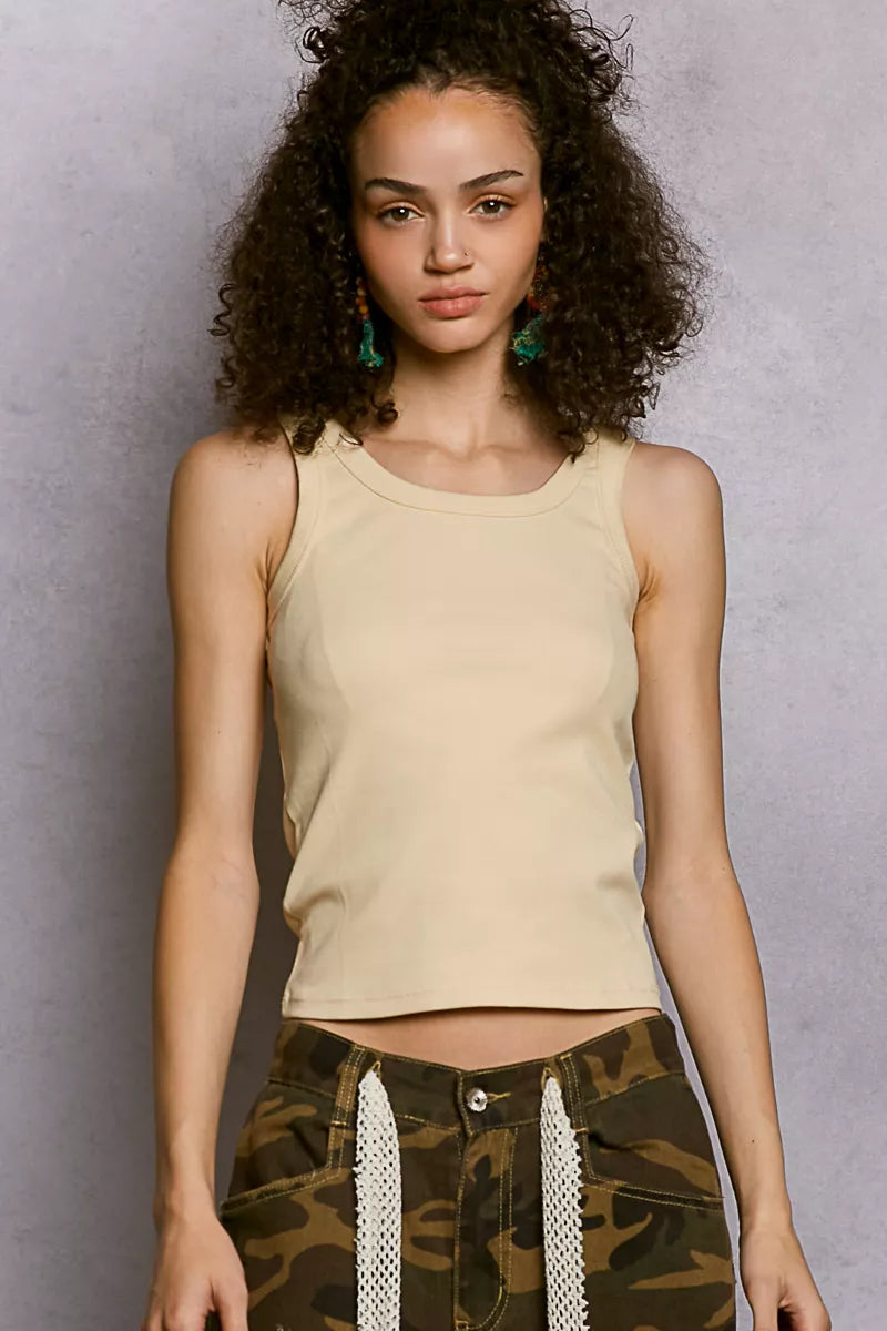 Woman wearing a beige tank top and camouflage pants against a gray background
