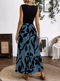 Woman wearing a black top and blue tiered skirt with black leaf pattern in a room.