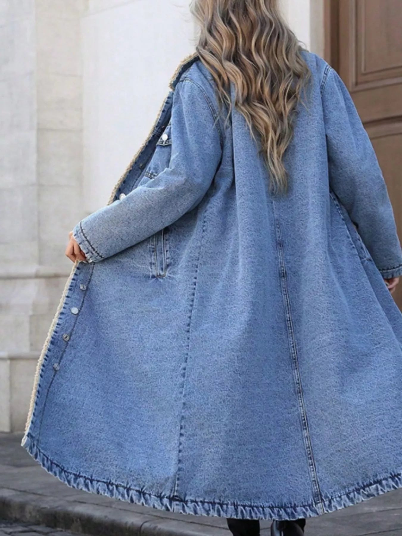 Long denim coat worn by a person with a blurred background