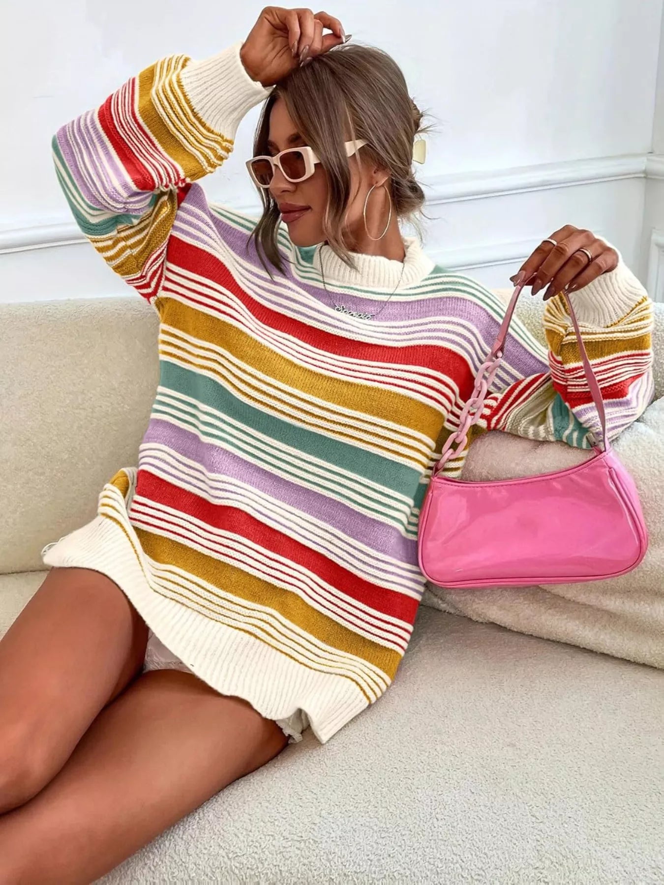 Person wearing a colorful striped sweater dress holding a pink handbag.