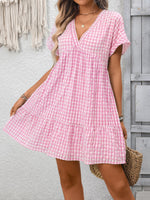 Woman wearing a pink checkered dress standing against a gray wall.