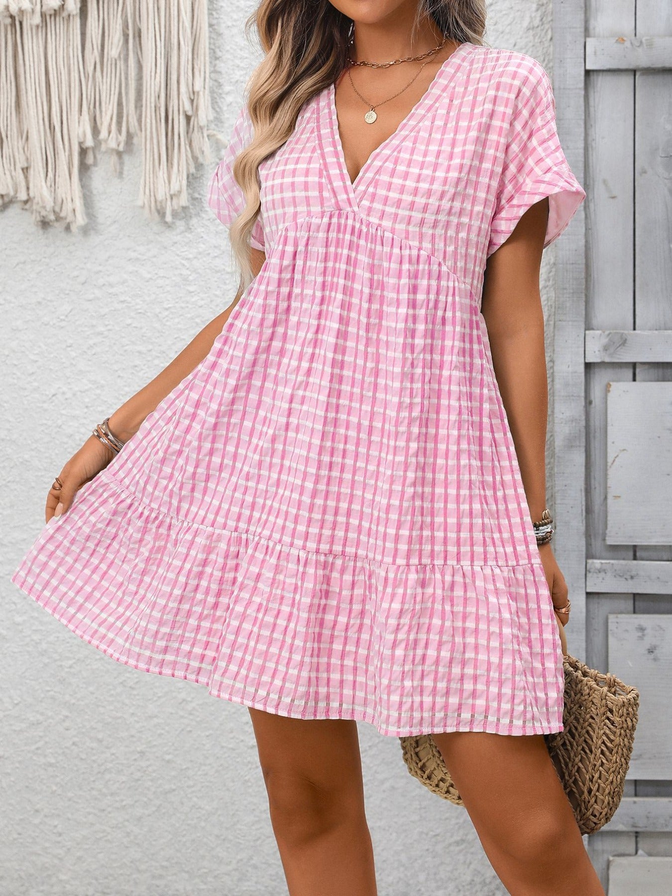 Woman wearing a pink checkered dress standing against a gray wall.