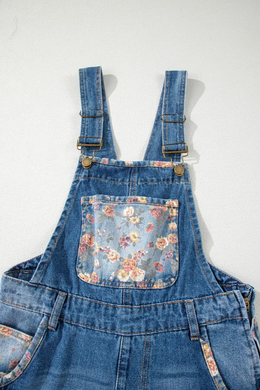 Blue denim overalls with floral pocket on a white background