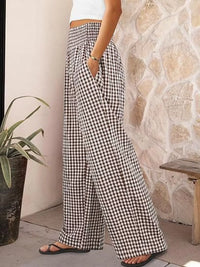 Person wearing black and white checkered pants standing against a stone wall.