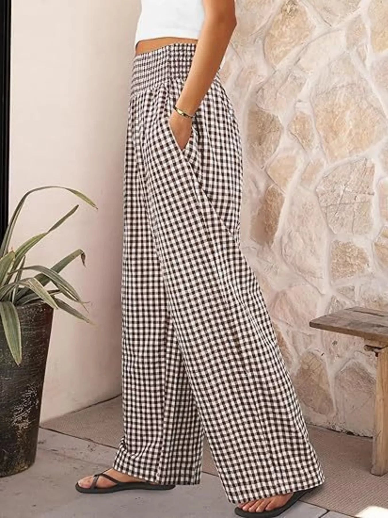 Person wearing black and white checkered pants standing against a stone wall.