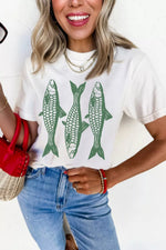 Woman wearing a white t-shirt with green fish graphics and blue jeans, holding a red bag.