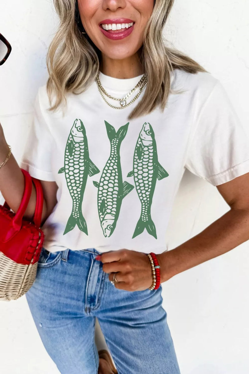 Woman wearing a white t-shirt with green fish graphics and blue jeans, holding a red bag.
