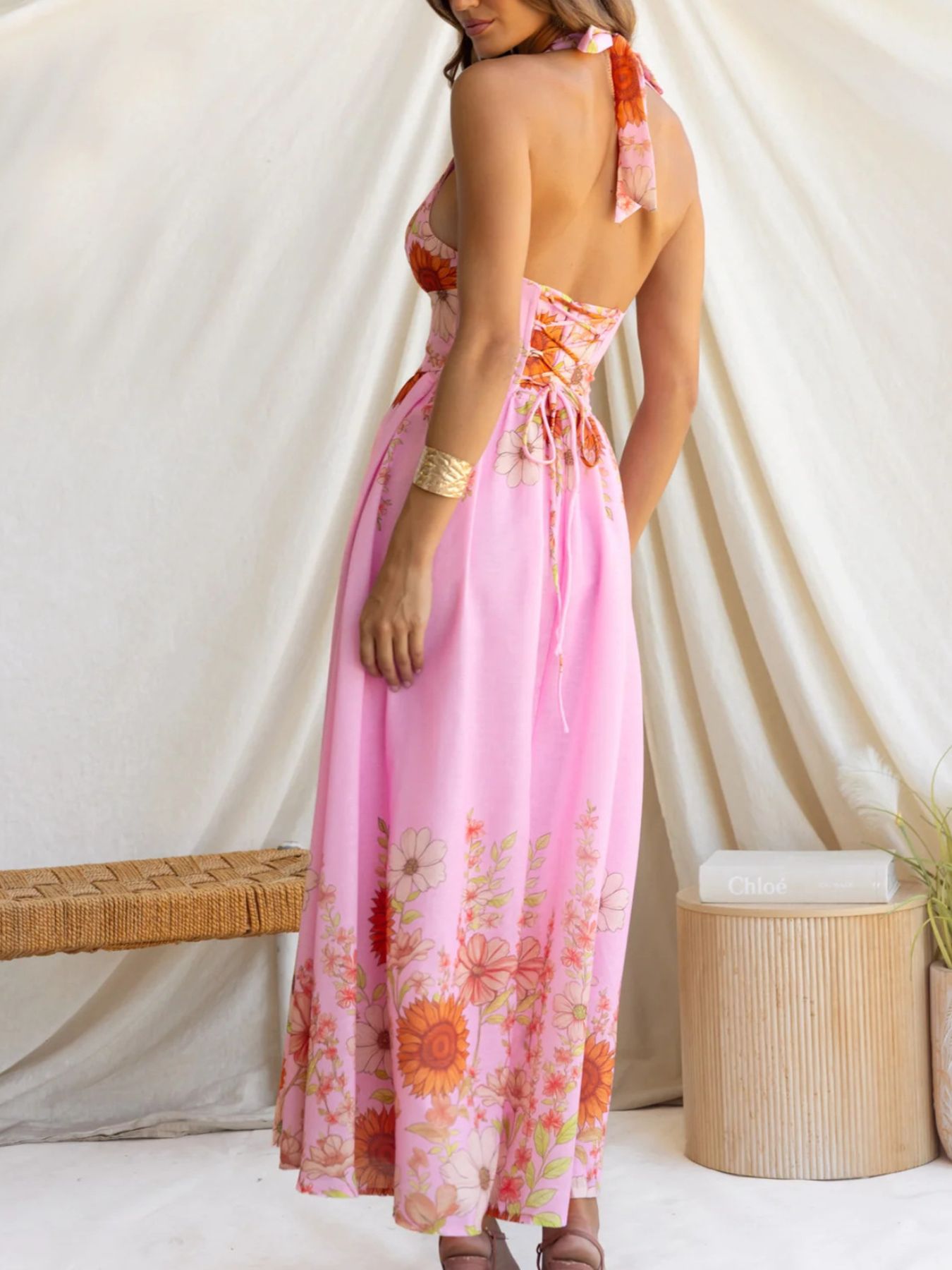 Woman wearing a pink floral dress against a white curtain background