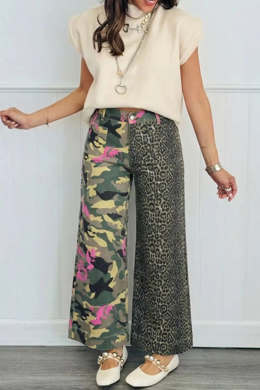 Person wearing a cream sleeveless top and patterned pants against a white wall.