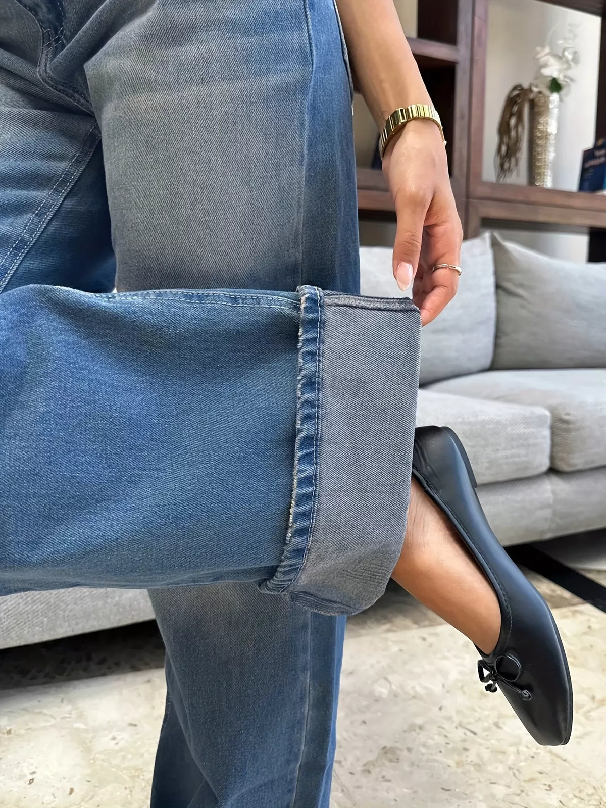 Person wearing blue jeans and black shoes in a living room setting