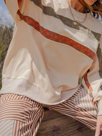 Person wearing a patterned top and beige pants with a blurred background
