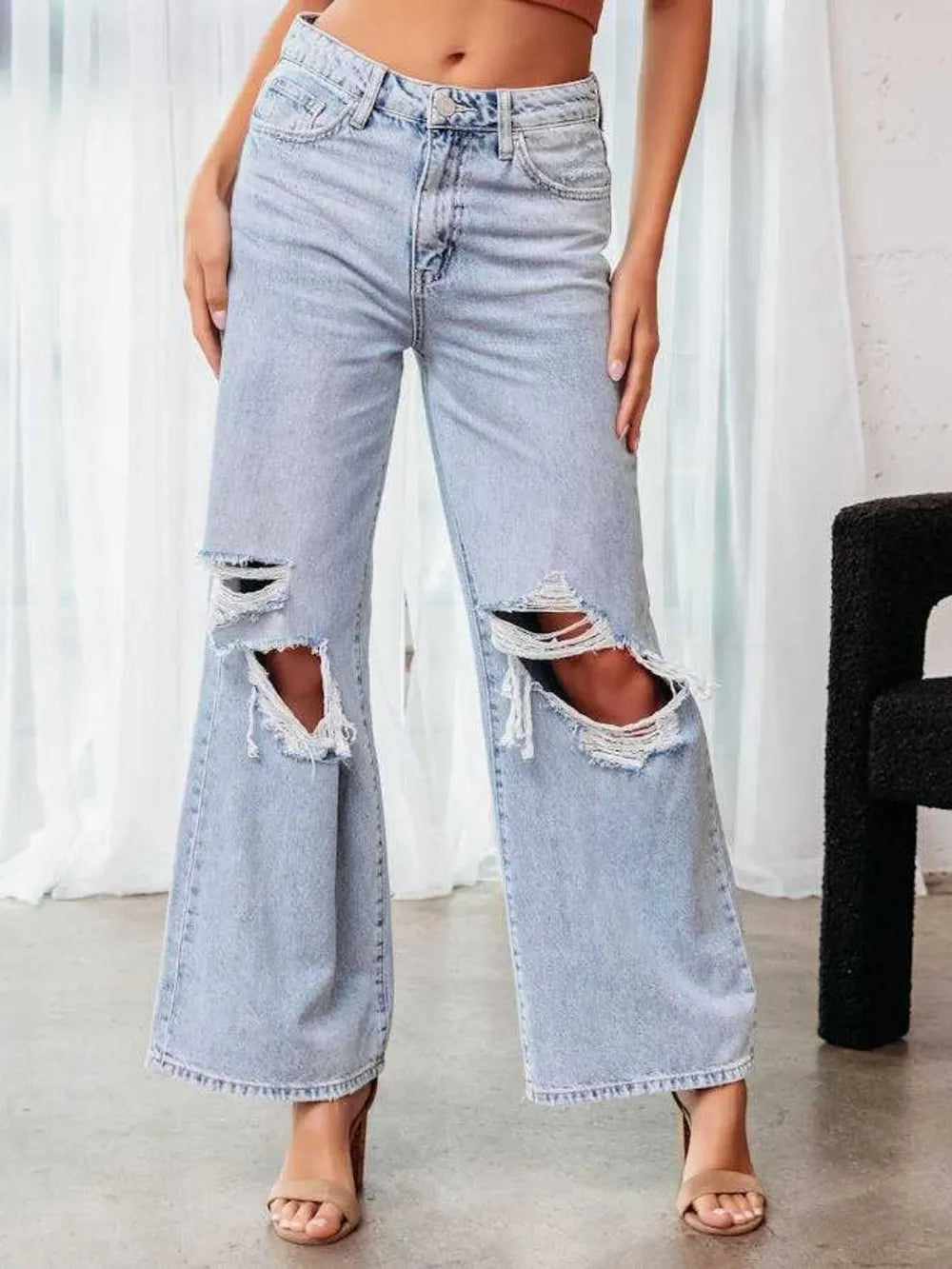Person wearing light blue ripped jeans in a minimal indoor setting