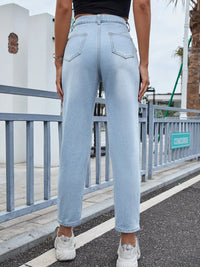 Person wearing light blue jeans standing on a street with a metal railing and building in the background.
