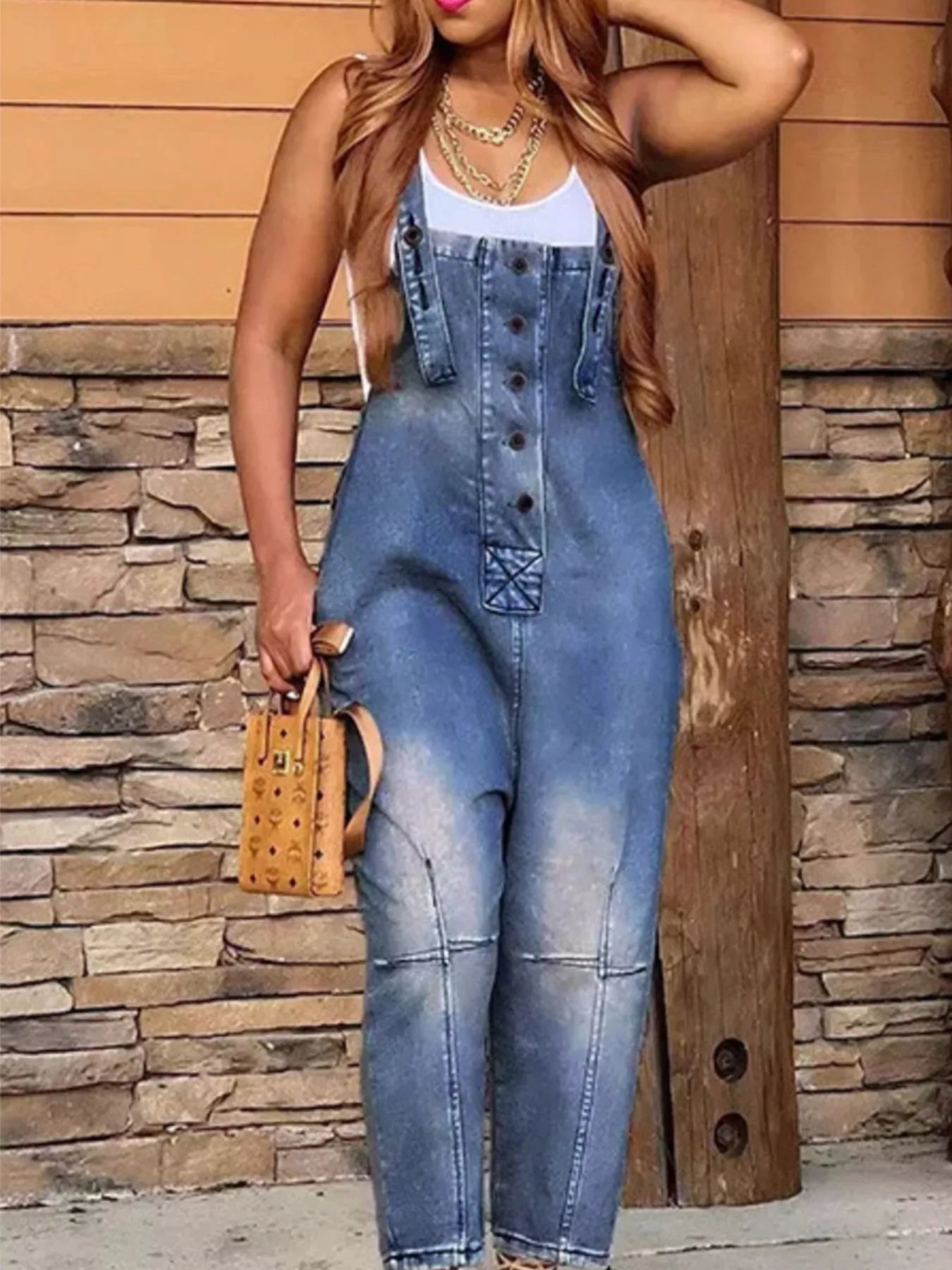 Person wearing a denim jumpsuit against a stone wall background