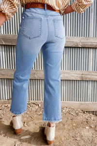 Person wearing blue jeans and a patterned shirt standing in front of a corrugated metal wall.