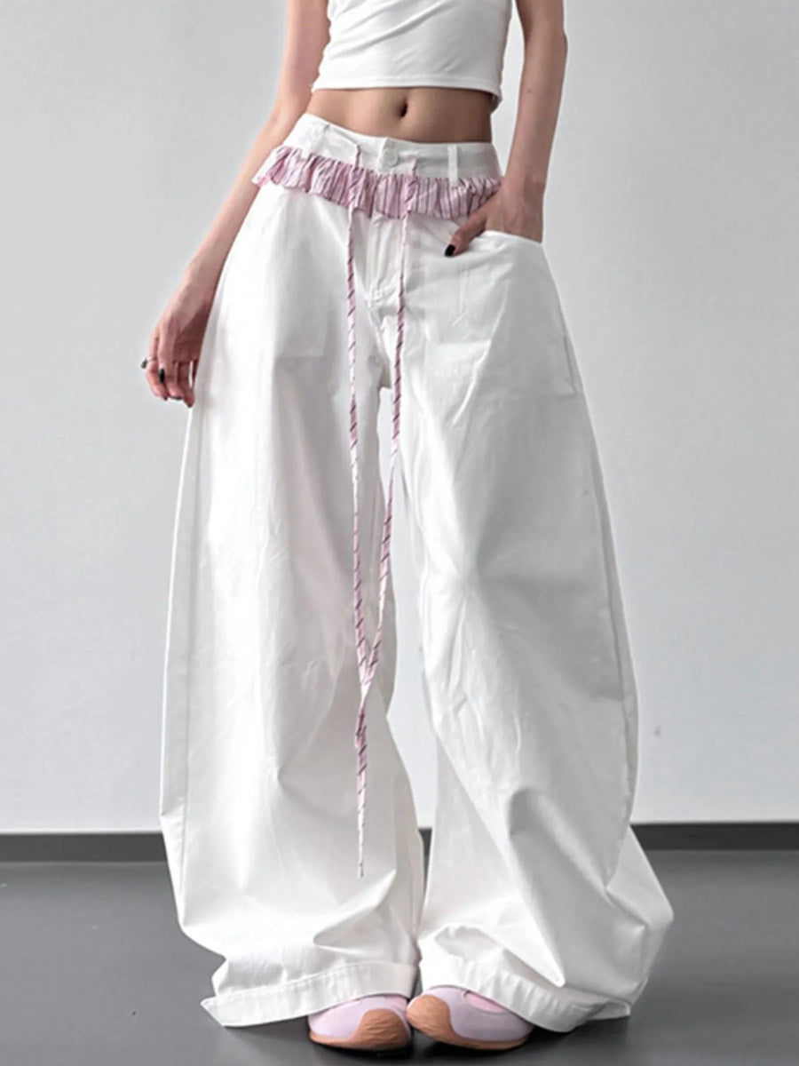 Person wearing white wide-leg pants with pink trim on a plain background