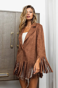 Woman wearing a brown suede jacket with fringe details indoors.