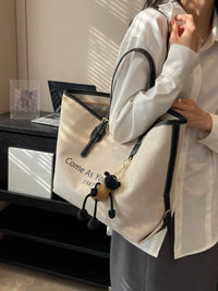 Person holding a beige tote bag with text and a black strap, standing in an indoor setting.