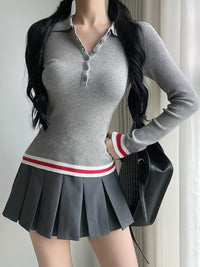 Person wearing a gray ribbed sweater and pleated skirt with a black handbag indoors.