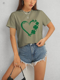 Person wearing a green t-shirt with a shamrock design and denim shorts against a gray background