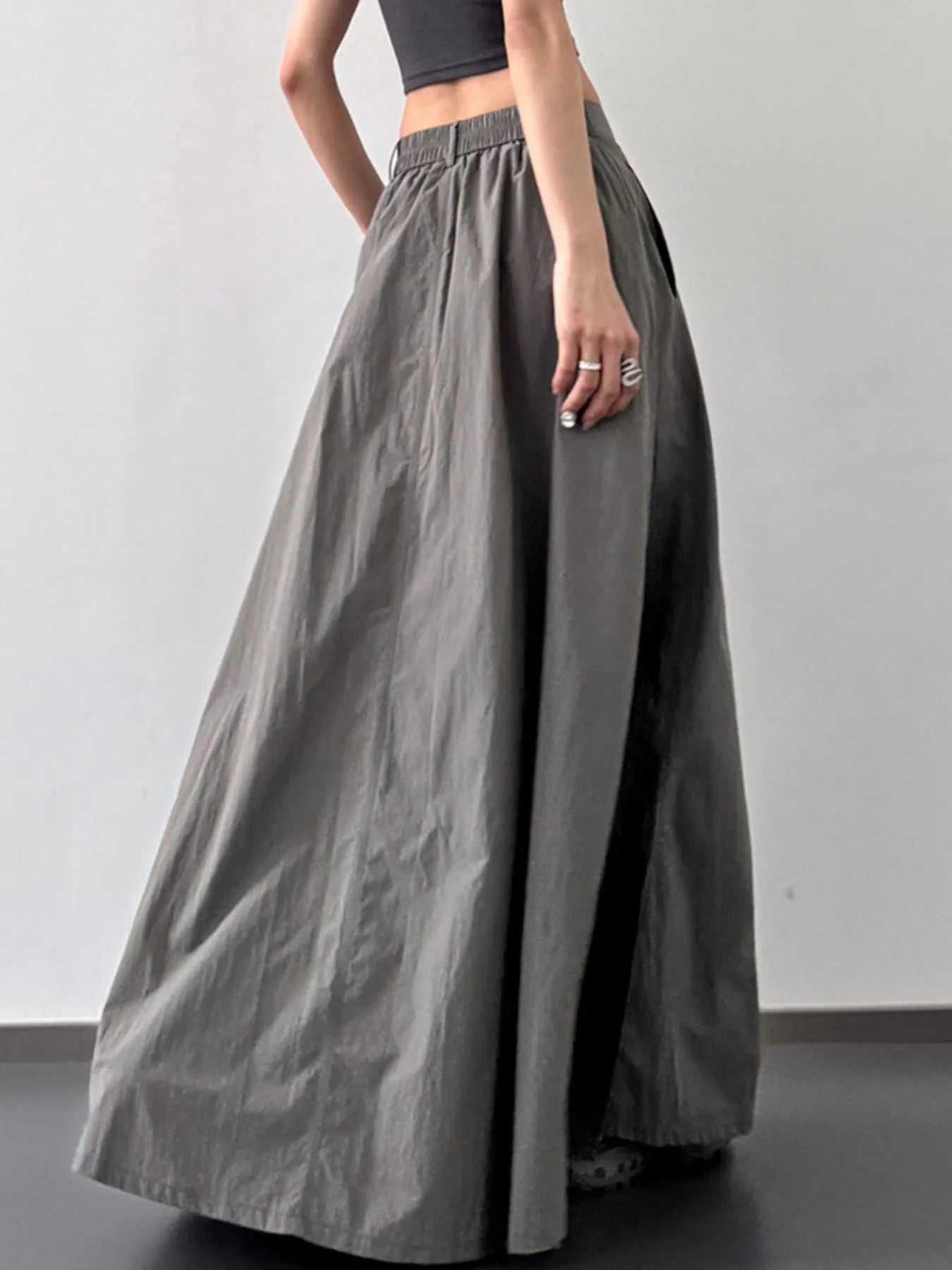 Person wearing a long gray skirt with a plain background