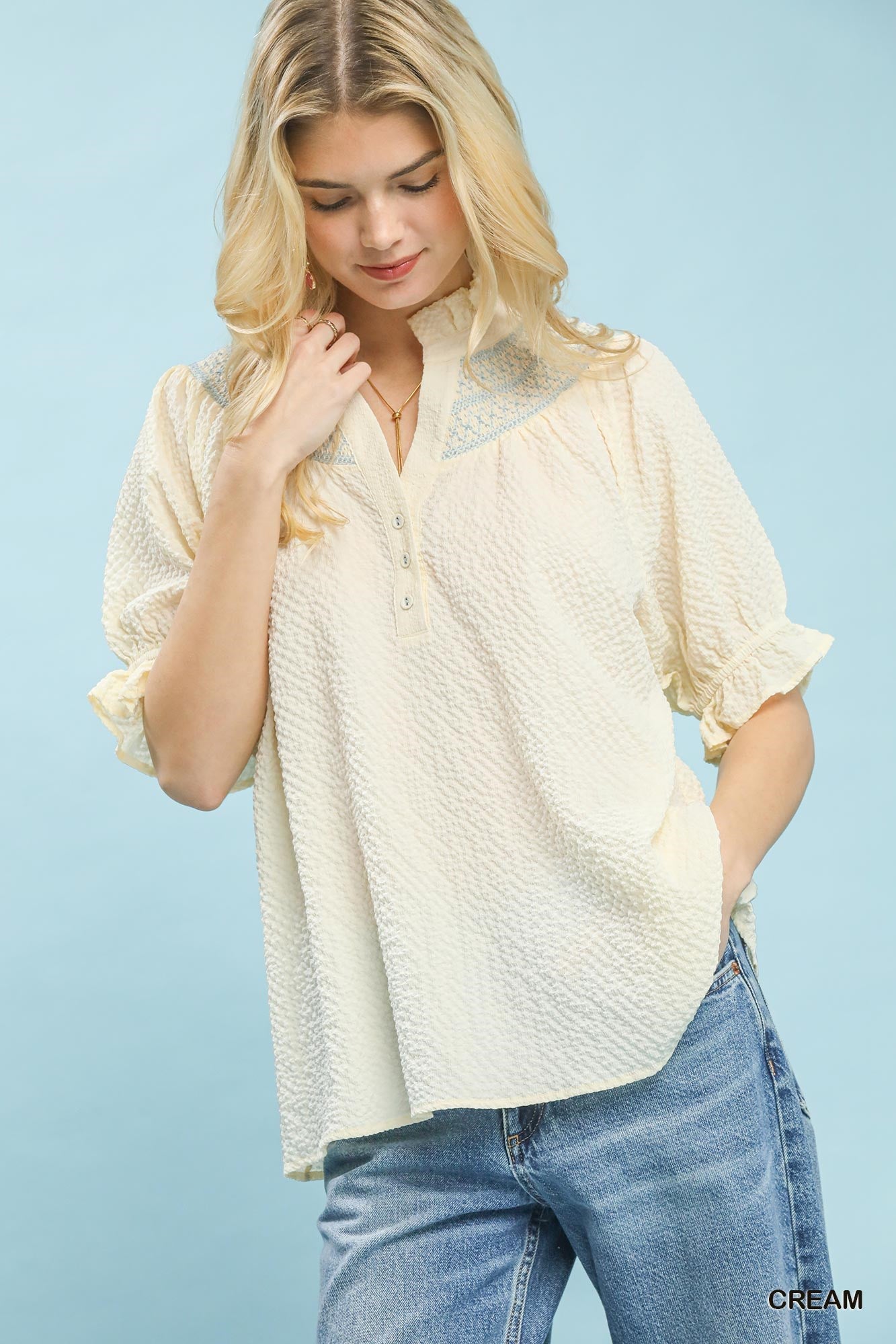 Woman wearing a cream blouse and blue jeans against a light blue background