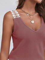 Close-up of a person wearing a mauve tank top with lace straps and layered necklaces on a light gray background.