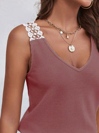 Close-up of a person wearing a mauve tank top with lace straps and layered necklaces on a light gray background.